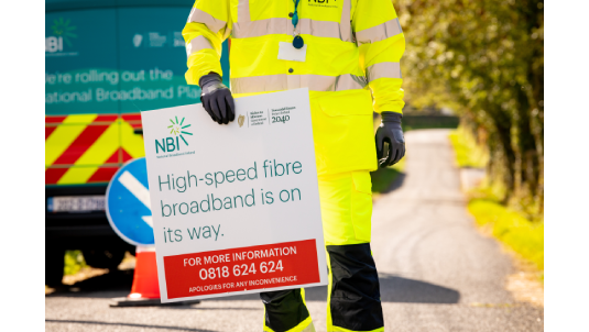 Worker holding a sign with "High speed broadband is on the way" wrote on it